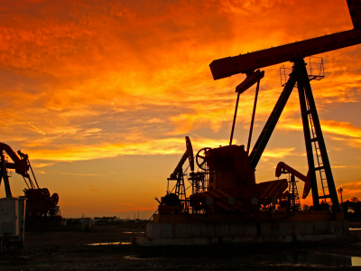 Plataformas de extração de petróleo em campo aberto ao pôr do sol, simbolizando a dependência de combustíveis fósseis no contexto da transição energética.
